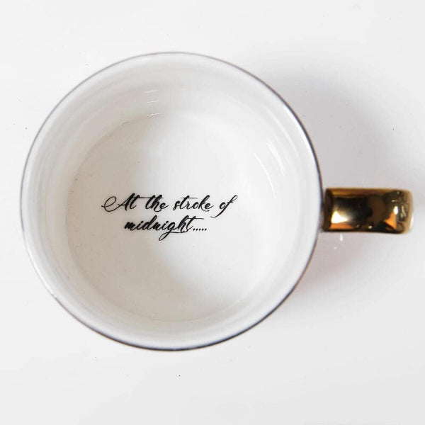 White mug with gold handle and text 'At the stroke of midnight' on a white background