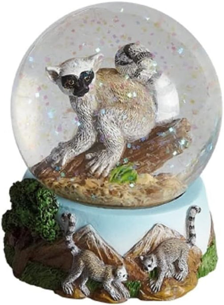 A lemur-themed snow globe featuring a large clear globe with a detailed adult lemur figurine, glitter inside, and a light blue base decorated with smaller lemur figures and rocky terrain.