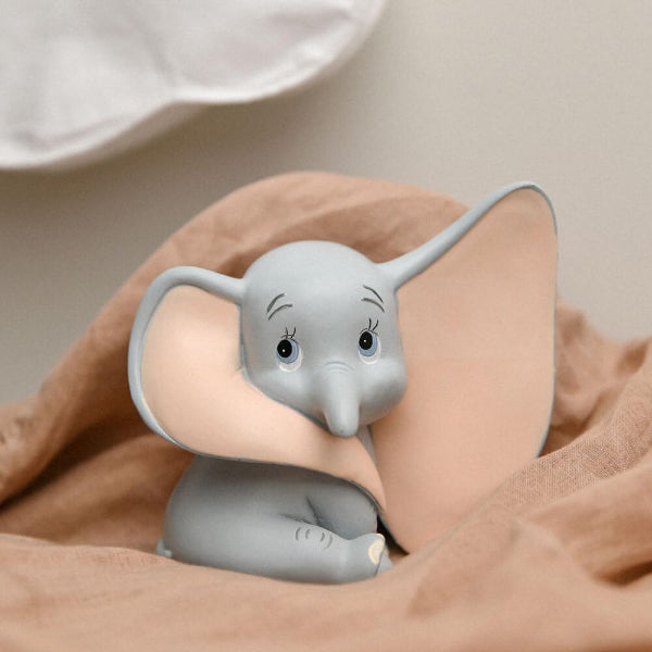 Small elephant plush toy peeking out from behind a brown blanket