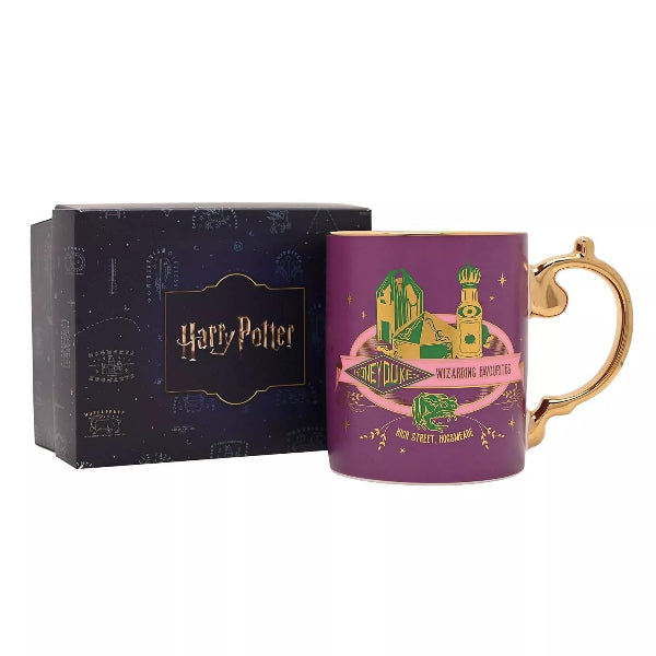 A purple Harry Potter mug with a gold handle and gold rim, featuring a Hogwarts-themed illustration and 'The Forbidden Forest' text, shown next to its dark blue presentation box on a white background.
