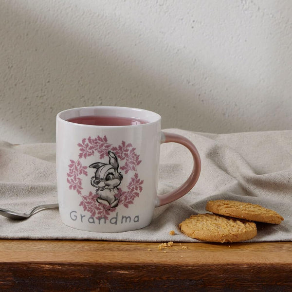 White mug with 'Grandma' and a rabbit design on a wooden surface with cookies and a spoon.