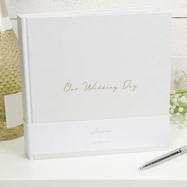 White wedding album with 'Our Wedding Day' text on a white surface with a pen and decorative items.