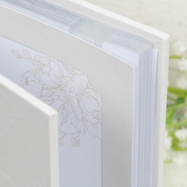 Close-up of a white book with floral embossing on the cover, blurred natural background