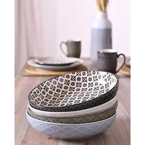 Set of three patterned ceramic bowls on a wooden table with cups and plates in the background.