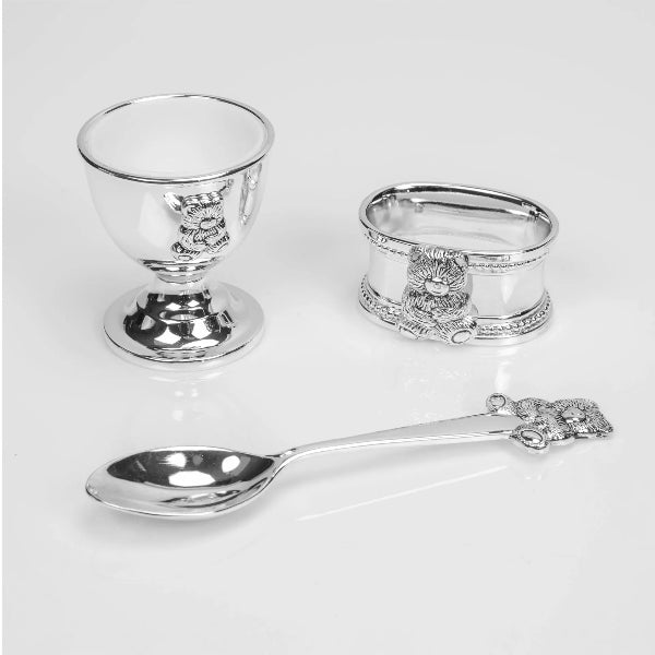 Silver egg cup, napkin ring, and spoon with decorative emblem on a white background