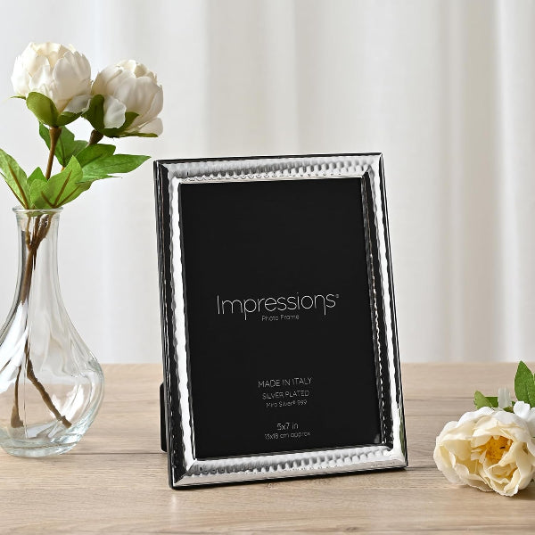 Silver photo frame with 'Impressions' branding on a wooden surface with flowers.