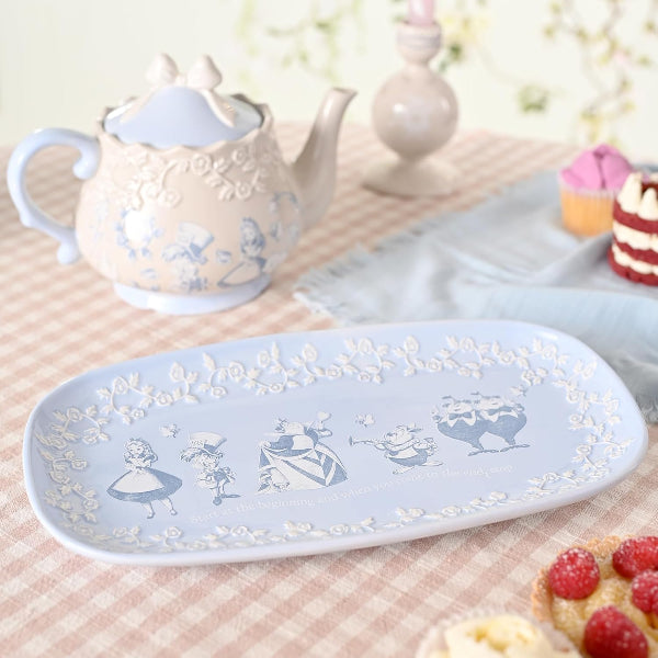 Decorative ceramic tray with floral and character design on a table with a teapot and pastries.