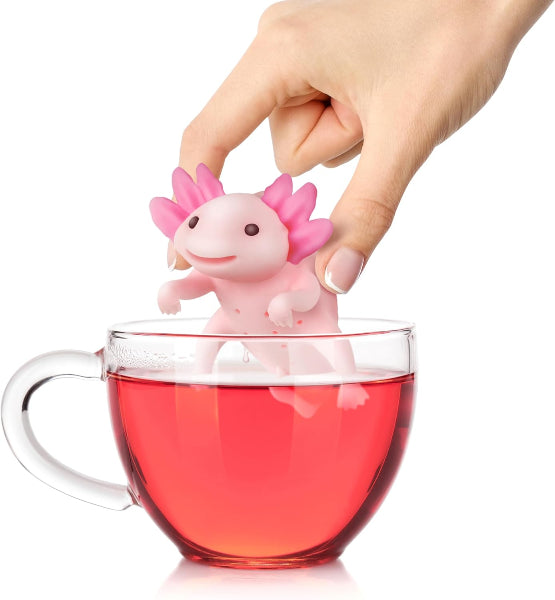 Pink axolotl-shaped tea infuser being placed into a glass of red liquid.