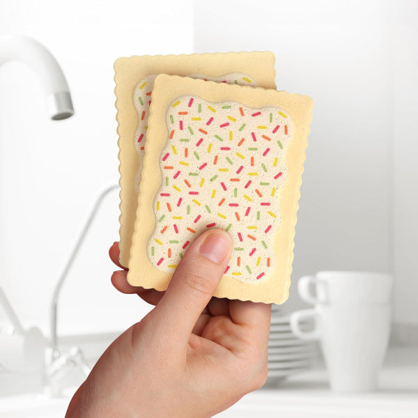 Hand holding a cookie-shaped product with sprinkles against a kitchen background