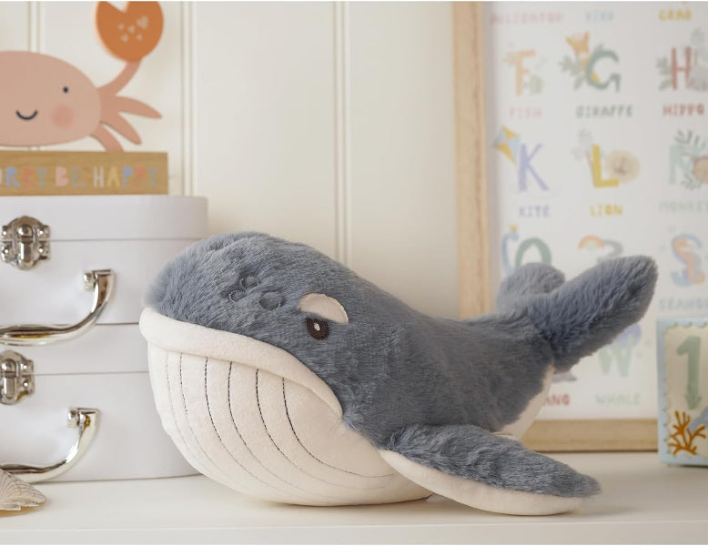 Plush whale toy on a white surface with decorative items in the background