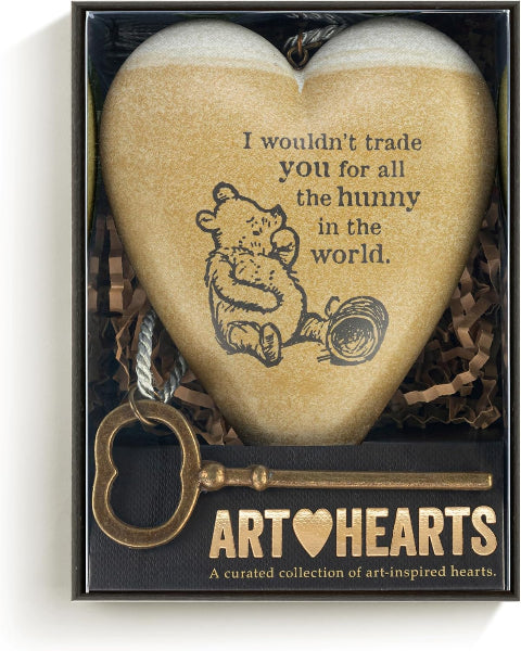 A heart-shaped stone ornament in a gift box, printed with a bear illustration and the quote 'I wouldn't trade you for all the hunny in the world.' A decorative key hangs from the box, and the front of the packaging reads 'ART HEARTS'.