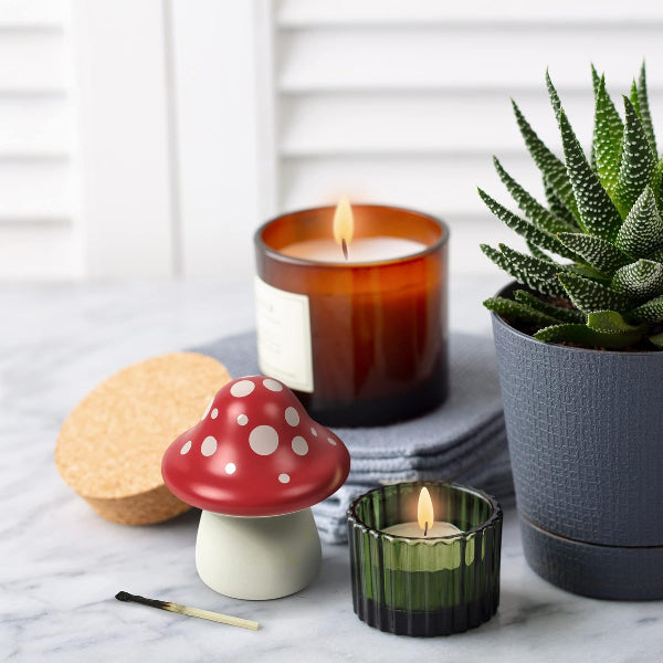 Candle in a red mushroom-shaped holder with a potted plant and match on a marble surface.