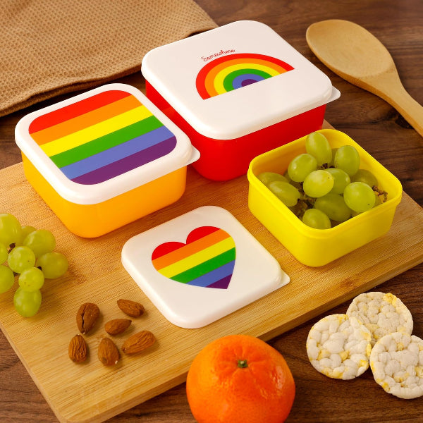 Set of colorful snack containers with rainbow designs on a wooden surface with snacks.