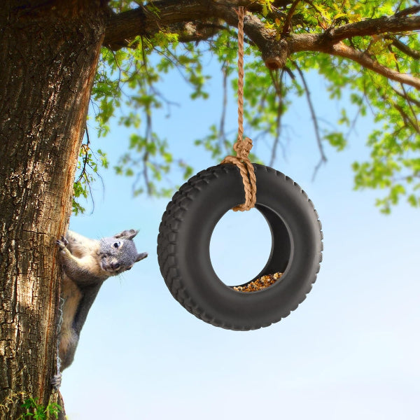Squirrel climbing a tree next to a tire swing with seeds.