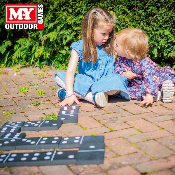 Two children playing with dominoes on a paved area with MY Outdoor Games logo.