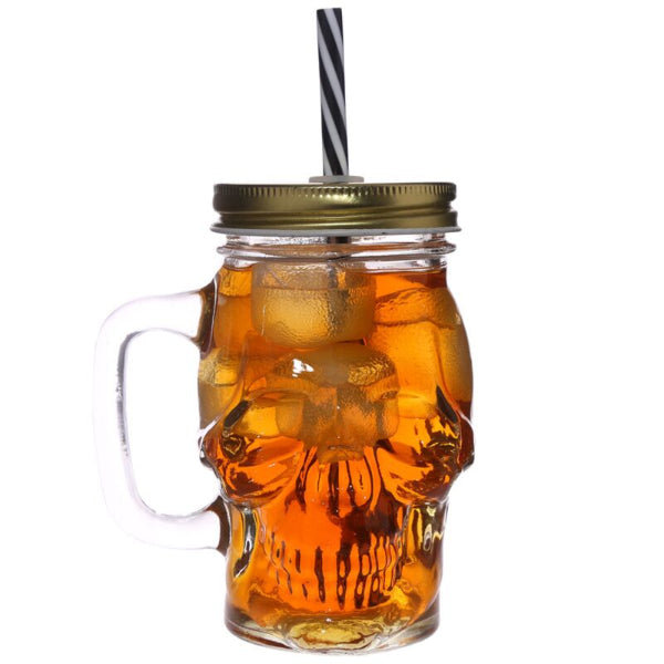 Skull-shaped glass mug with handle, gold lid, and straw filled with iced tea on a white background