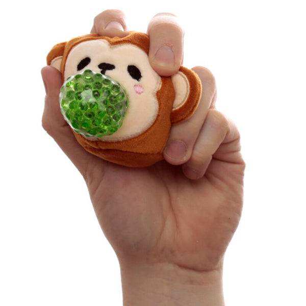 Hand holding a monkey-shaped stress ball with a green bead inside against a white background