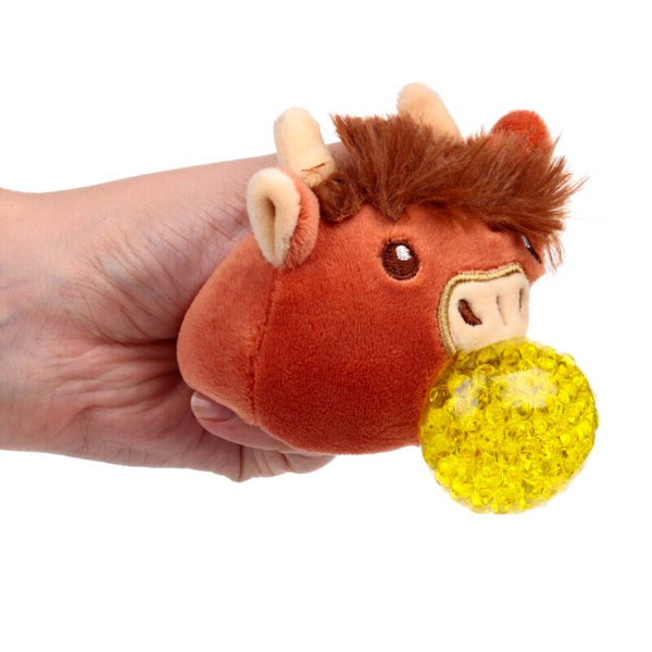 Plush toy resembling a bull with a yellow ball in its mouth, held by a hand on a white background
