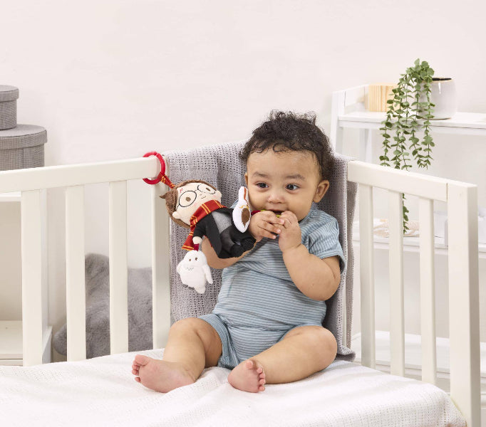 Baby sitting in a crib with toys, looking at the camera.
