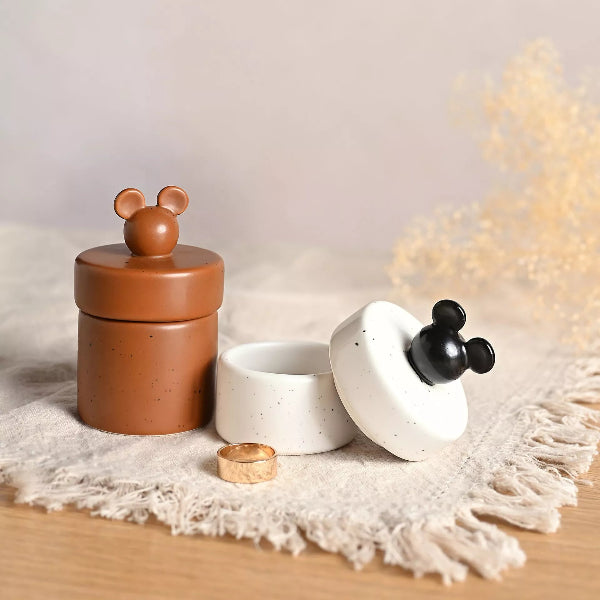 Two ceramic containers with animal-shaped lids on a textured surface