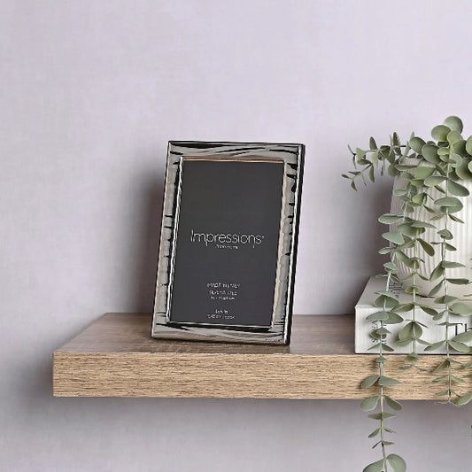 Silver photo frame labeled 'Impressions' on a wooden shelf with a plant in the background.