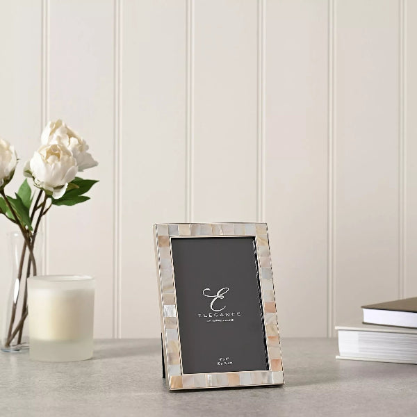 Decorative picture frame with 'Elegance' branding on a table with flowers and a candle.