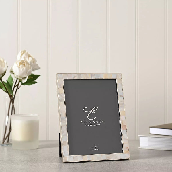 Decorative photo frame with 'Elegance' branding on a table with flowers and books in the background.