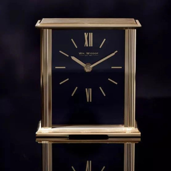 Decorative clock with gold frame and dark face on a reflective surface with dark background