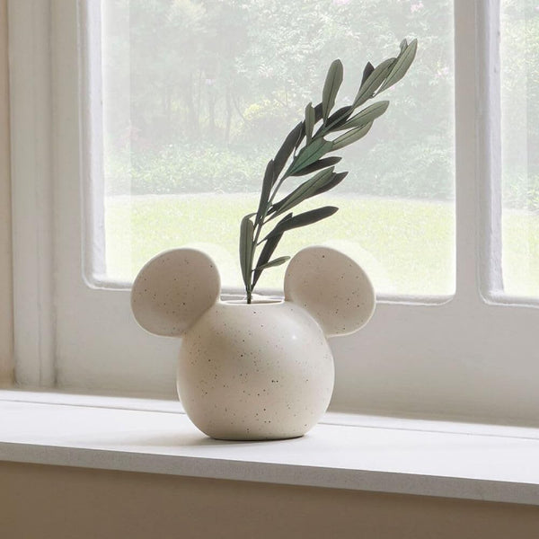 White speckled vase shaped like a mouse with a plant on a windowsill