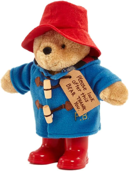 Stuffed toy bear in a blue coat, red hat, and boots holding a sign.