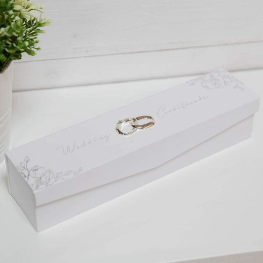White jewelry box with two wedding rings on a light wooden surface.