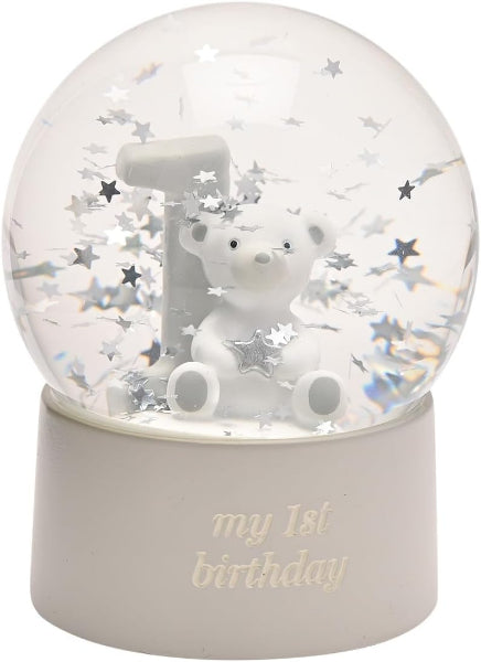 A clear glass or acrylic snow globe with a white bear and white letter '1' inside, surrounded by silver star confetti, sitting on a white cylindrical base engraved with 'my 1st birthday'.