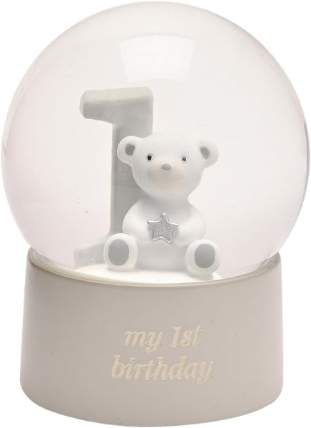 A white first birthday snow globe figurine featuring a small teddy bear holding a silver star next to a white number one, with the text 'my 1st birthday' on the base.