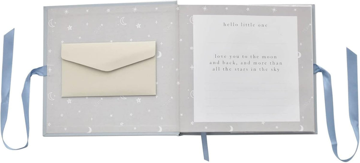 A baby keepsake album shown open, featuring a light gray cover with white moon and star patterns, a cream envelope in the left pocket, and a white card with printed text on the right page. Blue ribbon ties extend from both sides of the album against a white background.