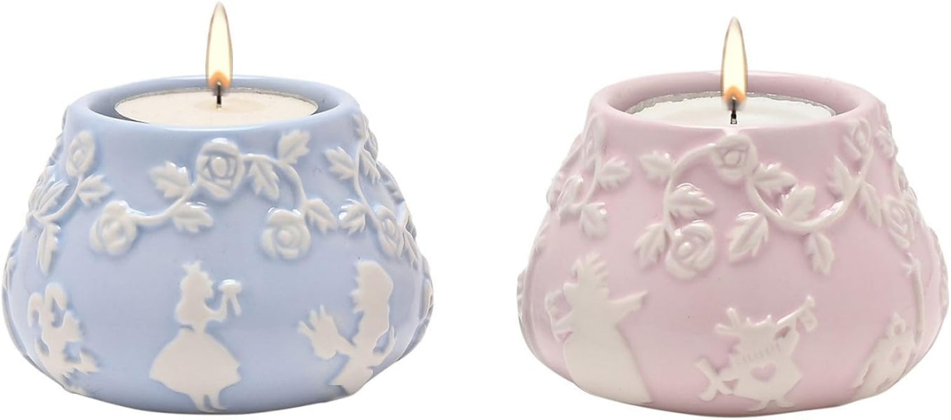 Two lit candles in decorative ceramic holders with floral patterns.