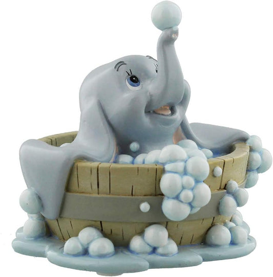 A Dumbo the Elephant bath figurine sitting in a wooden tub filled with white bubbles, holding a bubble ball in its trunk, on a white background.