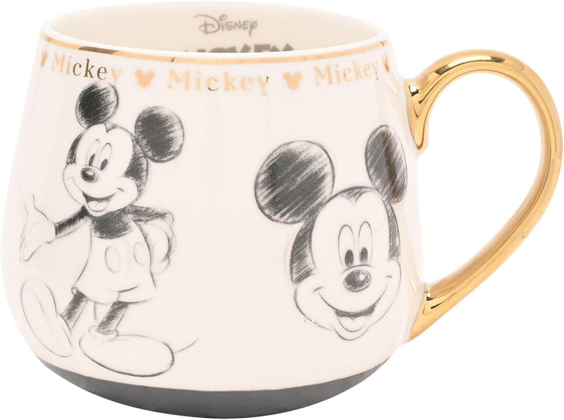 A Disney Mickey Mouse ceramic mug with a cream-colored body, black and white sketch illustrations of Mickey, gold trim, and a gold handle on a white background.