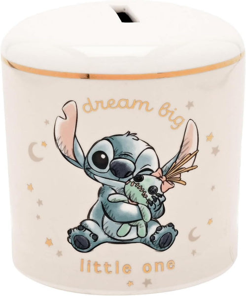 A ceramic piggy bank featuring a cartoon illustration of Stitch hugging a small plush toy, with the words 'dream big little one' printed in gold on a cream-colored background.