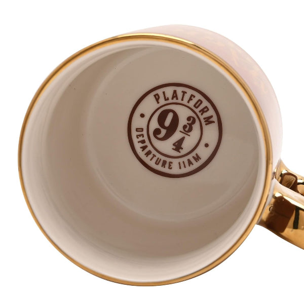 Close-up of the inside of a ceramic mug showing a printed 'Platform 9 3/4 Departure 11am' stamp in brown on a cream-colored interior, with a gold rim and a gold handle visible on the right.