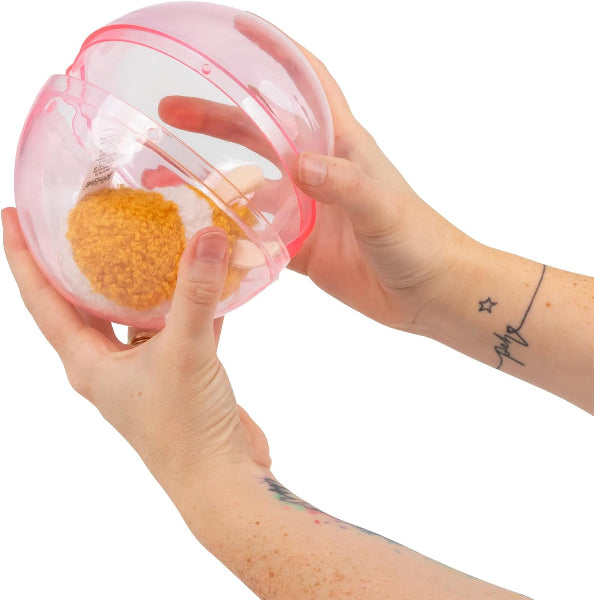A person's hands holding a translucent pink capsule-shaped container open to reveal a textured orange-brown powder or granule inside, set against a plain white background.