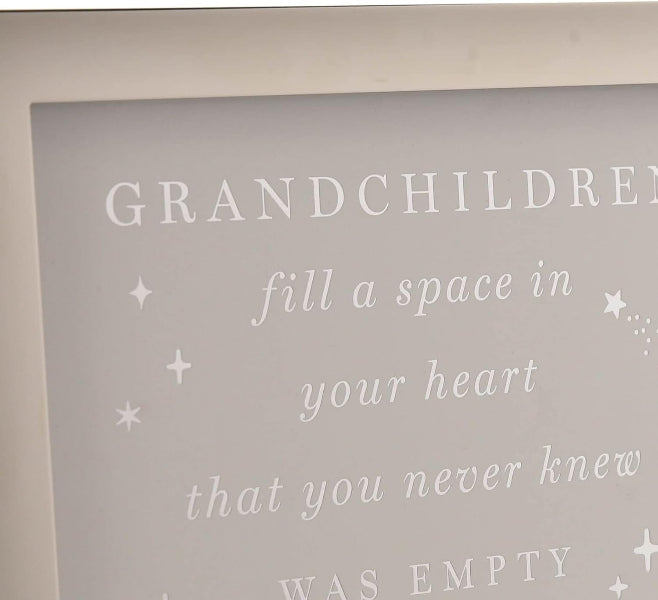 Close-up of a framed wall sign with a soft gray background and white lettering that reads 'GRANDCHILDREN fill a space in your heart that you never knew WAS EMPTY' with small star and dot accents.