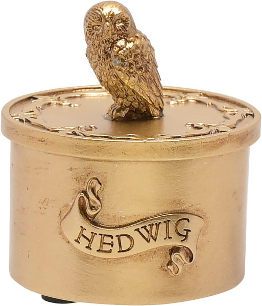 Gold-colored cylindrical object with an owl on top and 'Hedwig' engraved, on a white background