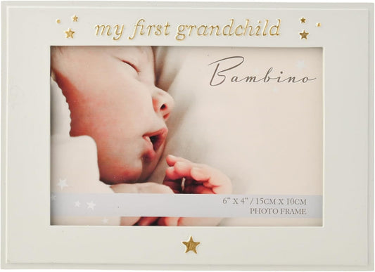 A square white photo frame with gold decorative text reading 'my first grandchild' and 'Bambino,' plus small gold stars. The center is a photo insert of a sleeping baby, and the bottom edge includes size text '6" x 4" / 15cm x 10cm PHOTO FRAME.