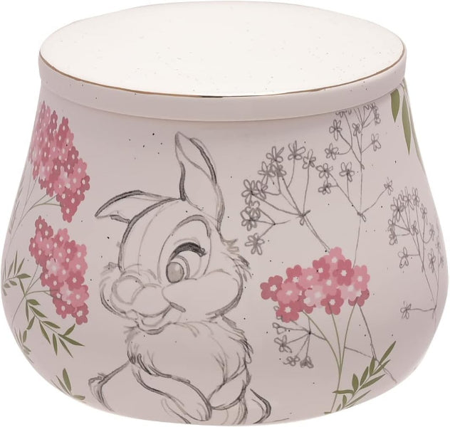 A round ceramic container with a lid, featuring a hand-drawn style illustration of a bunny surrounded by pink flowers and delicate botanical sketches on a speckled off-white background.