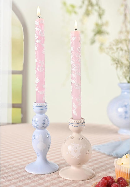 Two pink candles in decorative candlesticks on a table with a blurred background