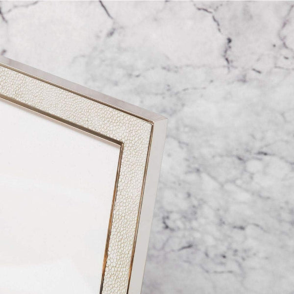Close-up of a picture frame corner with a textured cream border and a polished gold metal edge, set against a white and gray marble background