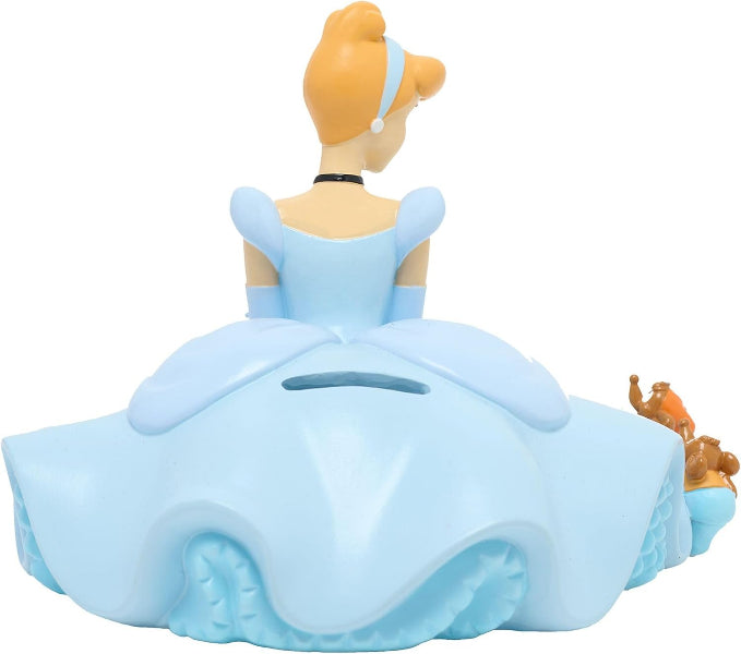 A Cinderella-themed plastic money box shaped like her dress, shown from the back with a gold-brown hair bun and a small coin slot on the back of the skirt. The dress is light blue, with a small brown and gold accessory figure beside it, all on a plain white background.