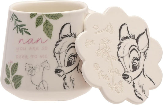 A ceramic mug with a matching flower-shaped lid, featuring Bambi the deer character and green leaf illustrations on an off-white background.