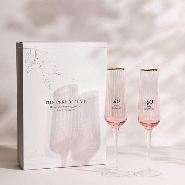 Two pink champagne flutes with gold accents next to a white box labeled 'The Perfect Pair' on a light background.