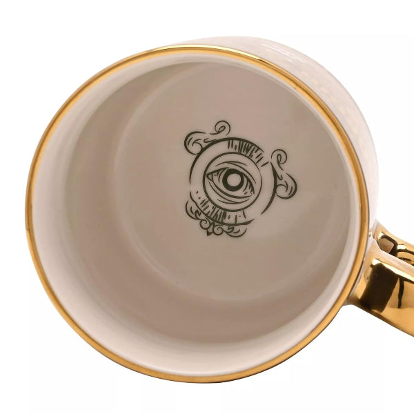 Beige mug with gold rim and handle featuring a black eye design on a white background